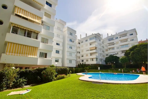 A residential building with a swimming pool surrounded by a well-maintained lawn.