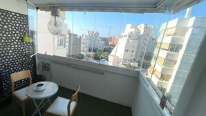 A balcony with a table and two chairs, a hanging light fixture, and a view of urban buildings.