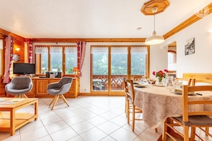 A cozy room with a dining table, chairs, a television, and a balcony with a view.