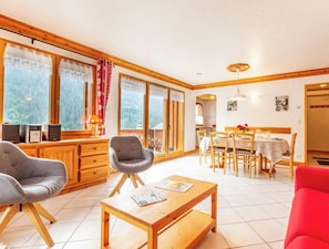 A spacious living area with wooden furniture, a dining table, and large windows offering a forest view.
