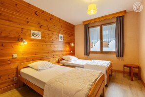Une pièce en bois avec deux lits, une fenêtre avec des rideaux et un petit tabouret.