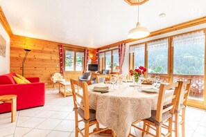 Un coin repas avec une table dressée pour quatre personnes, des chaises en bois, un canapé rouge et un téléviseur en arrière-plan.