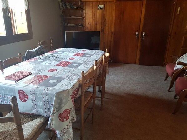 Un coin repas avec une table recouverte d’une nappe  à motifs, entourée de chaises en bois.