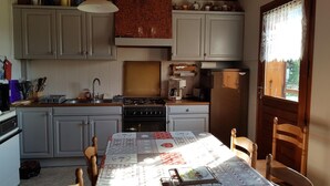 A kitchen with a central island, a dining table with a patterned tablecloth, and a view of the outdoors through a window. - LE CHAR - LA GIETTAZ (LA GIETTAZ)