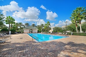 A swimming pool with a brick deck, palm trees, and lounge chairs. - 3BR Cozy Condo • Outdoor Veranda • Near Disney (Reunion)