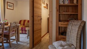 A cozy room with a wooden floor, a wicker chair, a bookshelf, and a dining area with a table and chairs.