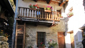A stone building with a wooden balcony, potted flowers, and a rustic entrance.