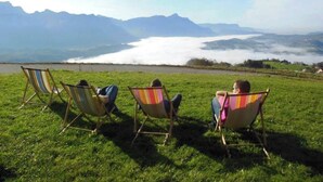 Tres personas sentadas en sillas de jardín coloridas a rayas en un campo de césped con vistas a montañas y un lago.