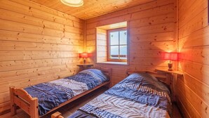 Una cabaña con dos camas de madera, un ventanal y una lámpara colgante.