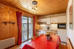 Un intérieur en bois comprenant une table à manger, un coin cuisine et une vue à travers une porte vitrée.
