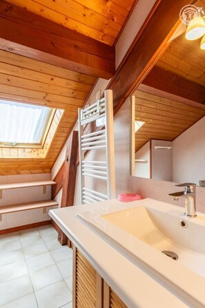 A modern bathroom with a skylight, wooden beams, a white sink, and a towel rack.