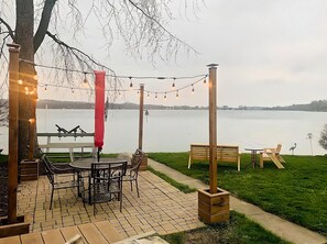 Un patio al aire libre con piso de ladrillo, sillas de metal, una mesa de madera y luces colgantes.