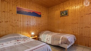 Een houten kamer met twee bedden, een nachtkastje met een lamp en twee ingelijste foto’s aan de wand.