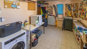 Een wasserette met een wasmachine, een droogrek en diverse spullen en materialen op planken en muren.