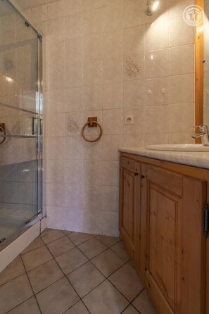 Un bagno con cabina doccia in vetro, mobile bagno in legno con lavandino e pavimento piastrellato.