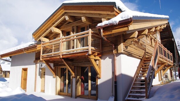 A wooden chalet with a balcony and a staircase leading to the upper floor, surrounded by snow. - LE REFUGE DU BACHAL N°1 (NOTRE DAME DE BELLECOMBE)