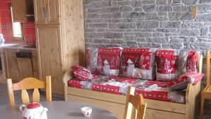 A cozy room with a wooden sofa covered in red and white patterned blankets, a dining table with a teapot and cup, and a stone wall in the background. - CHALET COCOON - ALBIEZ MONTROND (ALBIEZ MONTROND)
