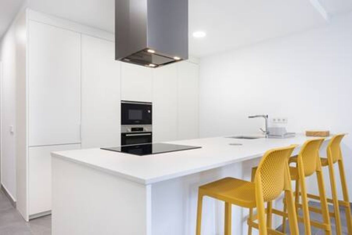 Una cocina moderna con muebles blancos, una isla central con taburetes de bar y un horno empotrado.