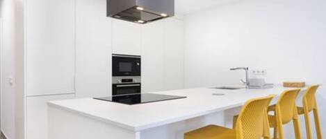 Una cocina moderna con muebles blancos, una isla central con taburetes de bar y un horno empotrado.