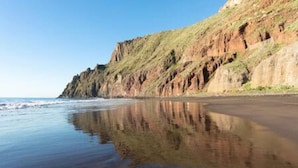 Une plage bordée d’une falaise rocheuse et aux eaux calmes.