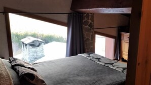 Un dormitorio con una cama litera, una ventana que ofrece vistas a un edificio de piedra y una lámpara sobre una mesita de noche.