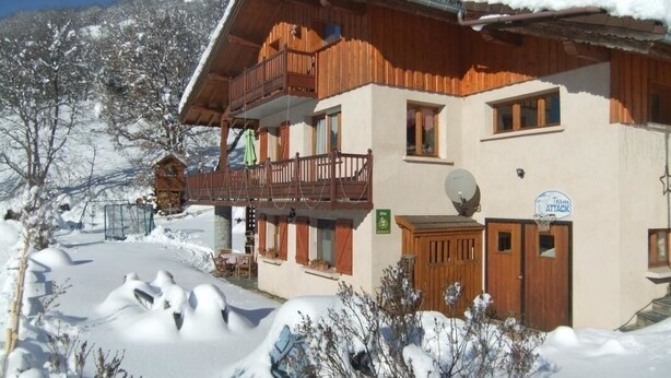 Eine Holzhütte mit Balkon, umgeben von schneebedeckten Bäumen und blauem Himmel.