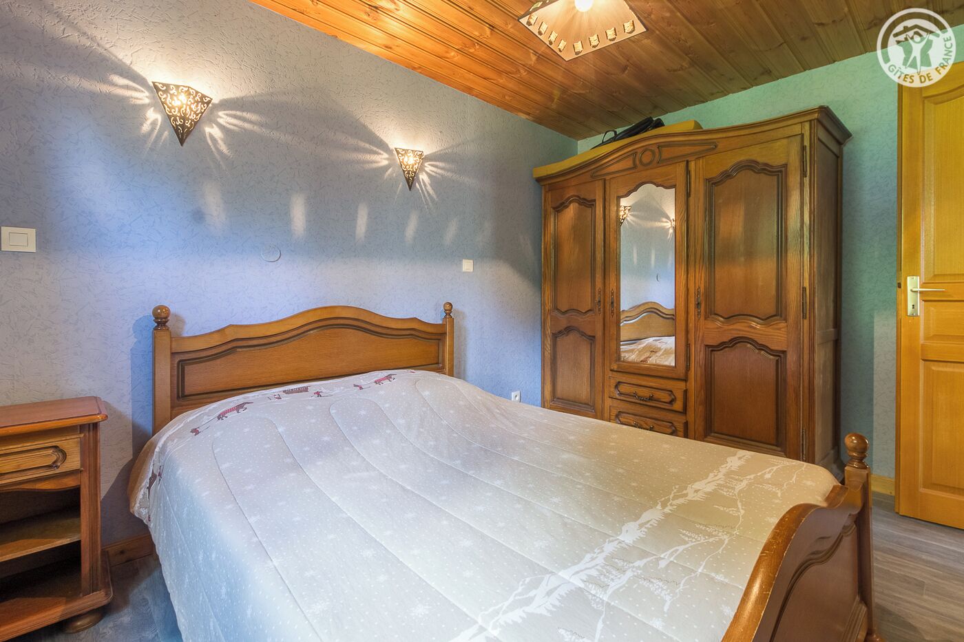 Un dormitorio con cama de madera, mesita de noche, armario y apliques de pared.