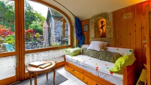 A cozy room with a wooden bench, a small table, and a bed with colorful polka dot bedding. - L'ARCHE - RUFFIEUX - Gîte (RUFFIEUX)