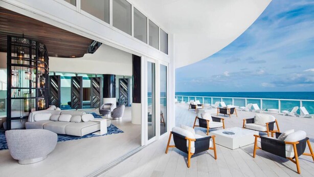 A modern outdoor lounge area with a white sofa, armchairs, and a dining table.