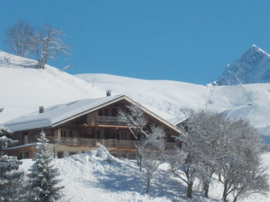 Un chalet en bois doté d’un balcon, entouré d’arbres couverts de neige et avec une montagne en arrière-plan.