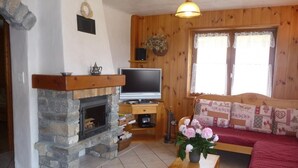 A cozy living room with a stone fireplace, a television, a wooden desk, and a comfortable sofa. - LE CHENET DES PIERRES (CHAMPAGNY EN VANOISE)