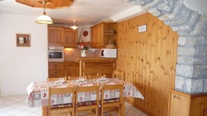 A cozy kitchen with wooden cabinets, a stone wall, and a dining table set for four. - LE CHENET DES PIERRES (CHAMPAGNY EN VANOISE)