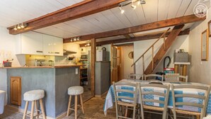 A rustic interior with a wooden ceiling, a kitchen area, a dining table with chairs, and a staircase. - LA COMBE DE MOULIN - PEISEY NANCROIX (PEISEY NANCROIX)