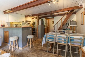 Een landelijke inrichting met houten plafond, een keukenhoek, een eettafel met stoelen en een trap.