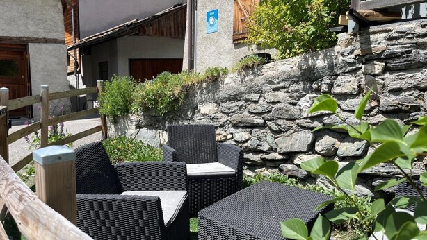 An outdoor seating area with wicker furniture, a stone wall, and a wooden fence. - LA COMBE DE MOULIN - PEISEY NANCROIX (PEISEY NANCROIX)