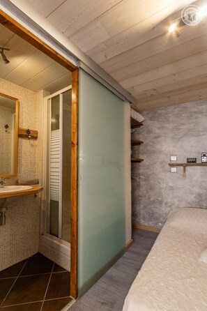 Un dormitorio con cama, una puerta de madera y un baño con lavamanos y espejo.