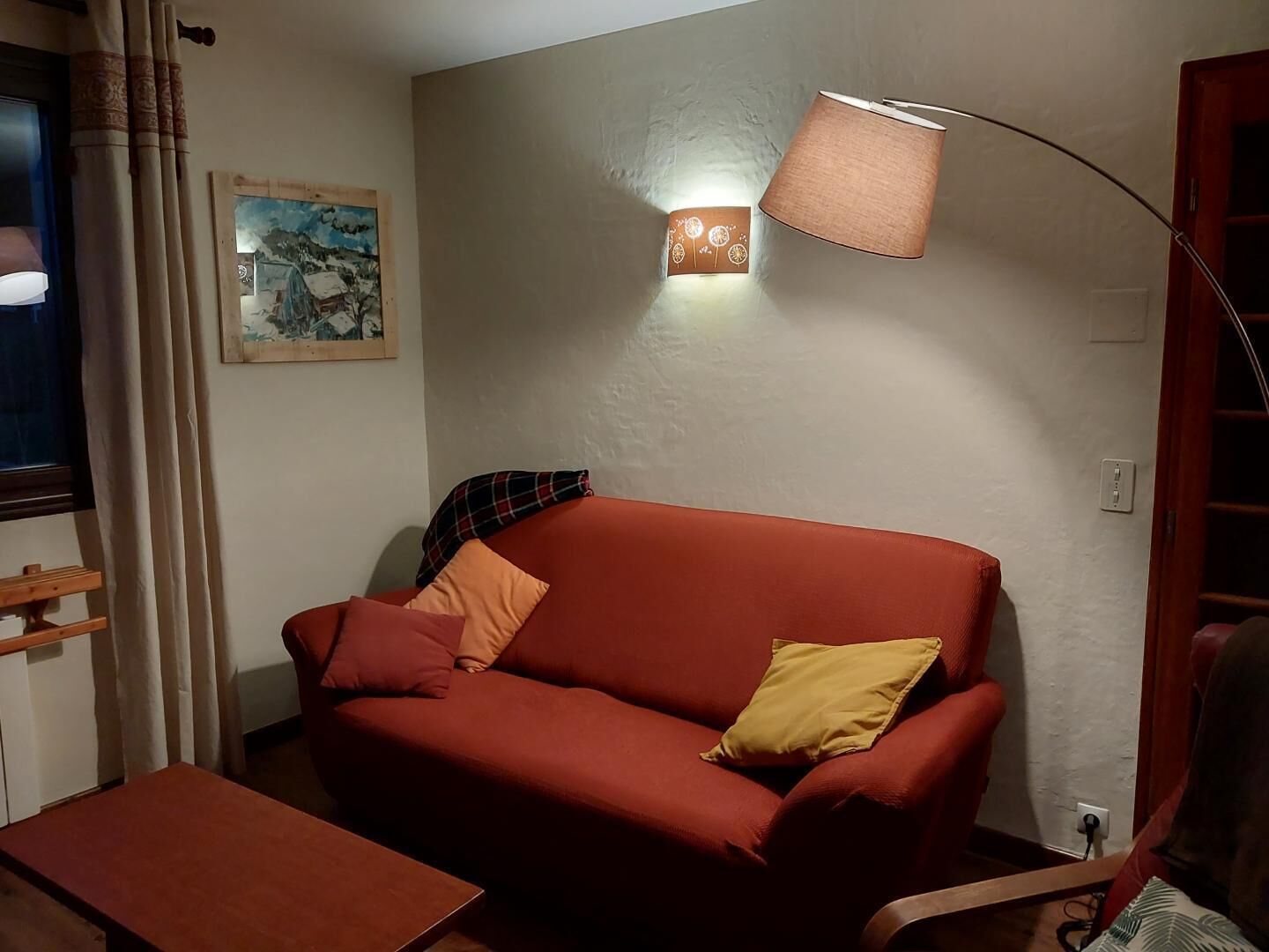 Una sala de estar acogedora con un sofá rojo, una mesita, una lámpara y un cuadro en la pared.