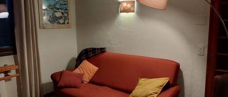 Una sala de estar acogedora con un sofá rojo, una mesita, una lámpara y un cuadro en la pared.