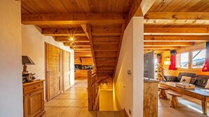 Ein Holzinnenraum mit einer Treppe zu einem Erkerbereich, einer Küche im Hintergrund und einer Sitzecke mit Tisch und Bänken.
