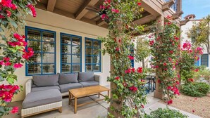 A covered outdoor seating area with a sofa and coffee table, surrounded by lush greenery and flowering plants. - Rejuvenating Desert Escape in La Quinta #A (La Quinta)
