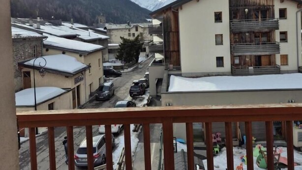 A mountain village with snow-covered buildings, a street with parked cars, and a view of snow-capped mountains.
