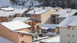 A residential area with snow-covered roofs and buildings, surrounded by trees and a mountain in the background.