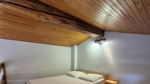 A single bed with a wooden headboard, a bedside table, and a wall-mounted light fixture in a room with wooden ceiling beams.