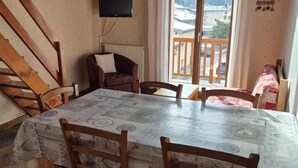 A dining area with a table and chairs, a television mounted on the wall, and a view of mountains through a window.