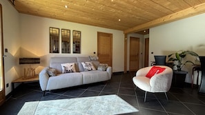 A living room with a sofa, a chair, a rug, and a wooden ceiling.