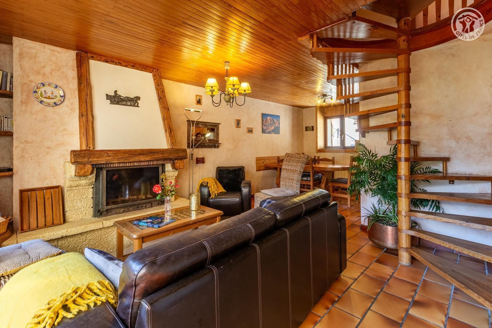 A cozy living room with a fireplace, leather sofa, wooden staircase, and a dining area.