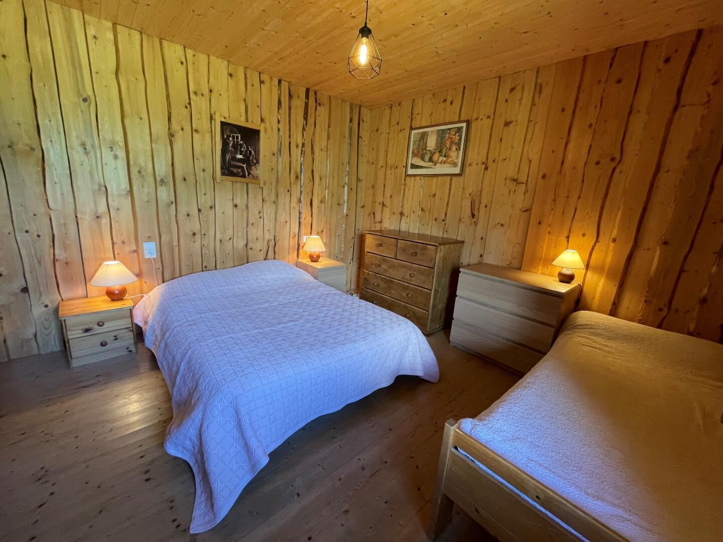 Una habitación acogedora de madera con dos camas, un aparador y dos mesitas de noche con lámparas.