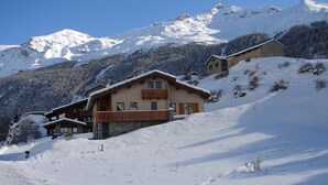 En byggnad i chalet-stil med en träbalkong, omgiven av snötäckta berg.