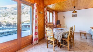 En stuga byggd av trä med ett matområde, stora fönster och utsikt över ett snötäckt landskap.