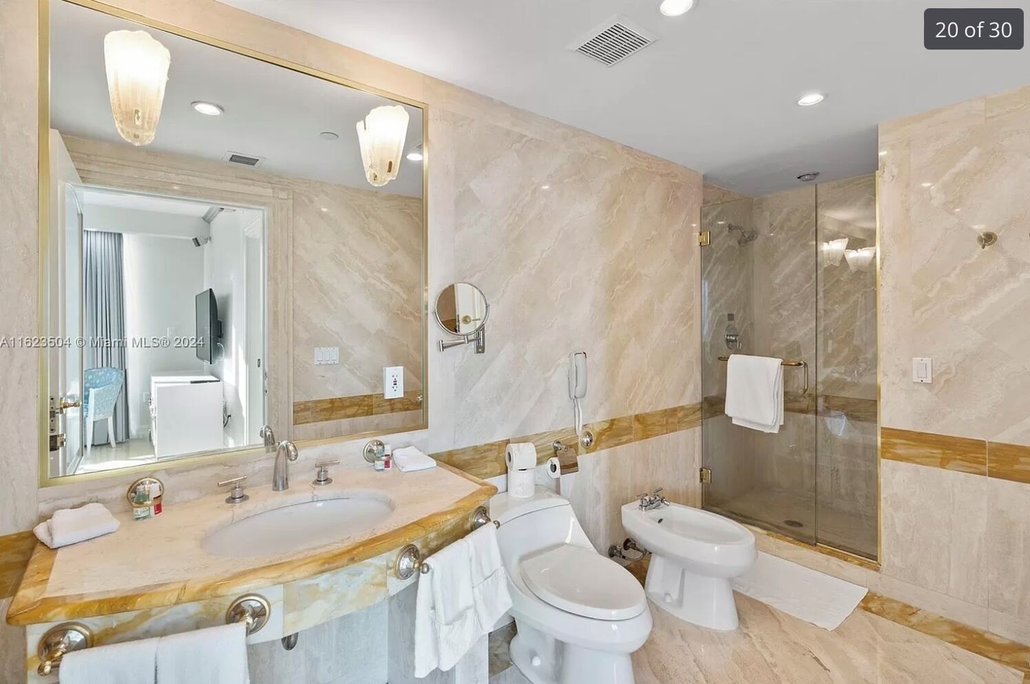 A modern bathroom with a large mirror, two sinks, a toilet, and a glass-enclosed shower.